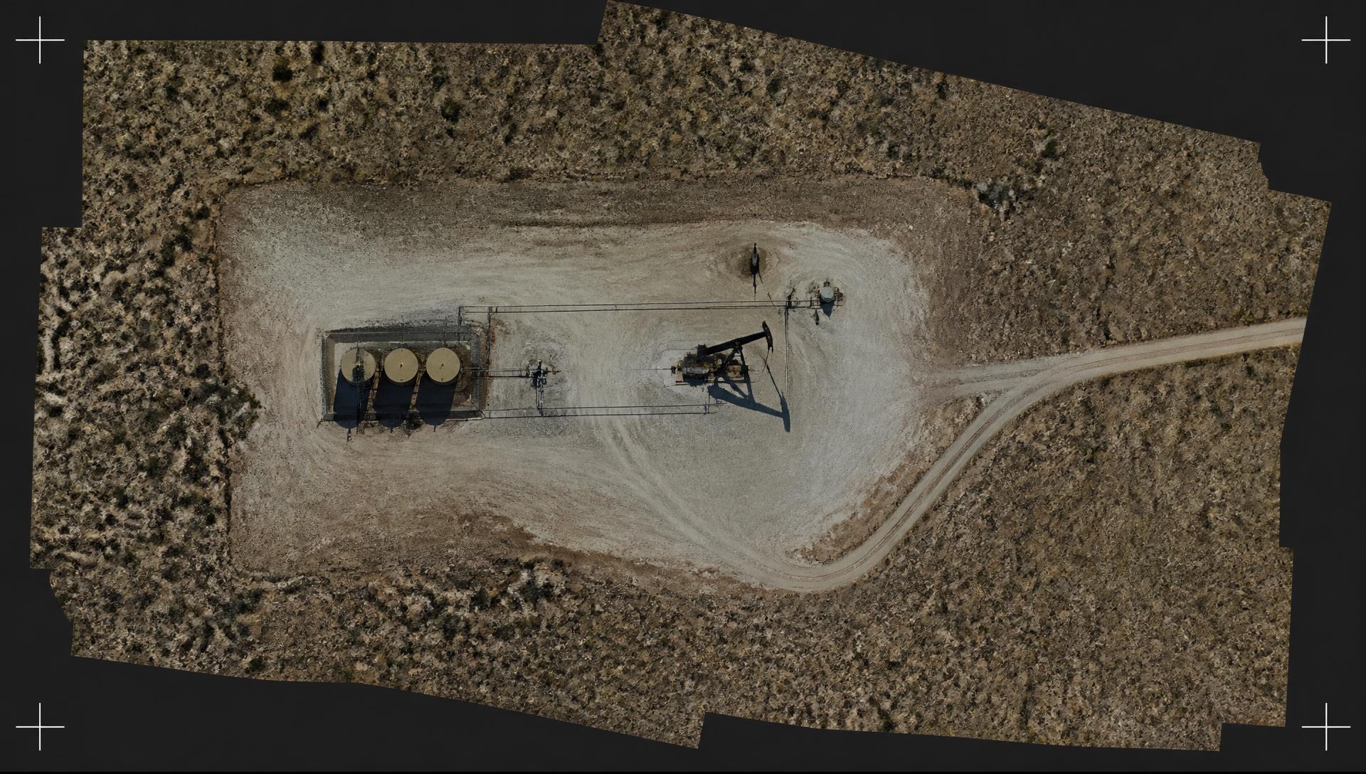 Top-down drone orthomosaic of a caliche well pad with pumpjack, tank battery, flowlines and access road